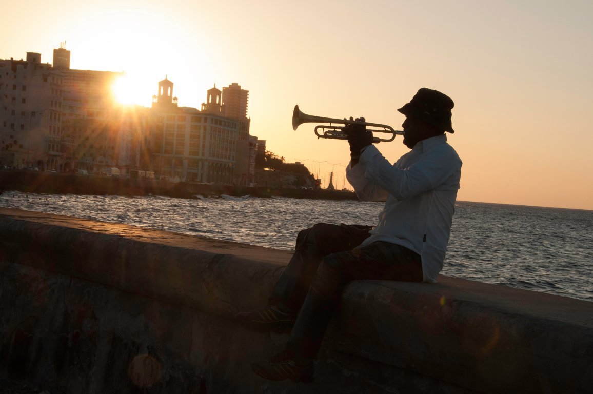 A musician plays trumpet on the Havana seawall at sunset